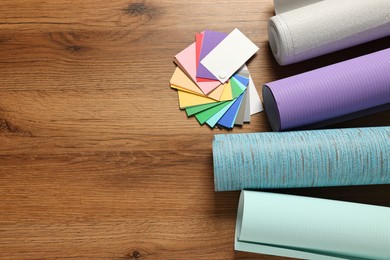 Different wallpaper rolls and color palette samples on wooden table, flat lay. Space for text