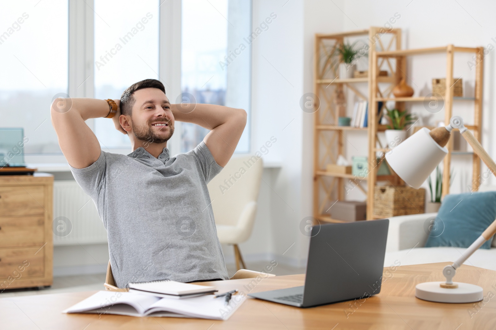 Photo of Happy man having break while working with laptop at wooden desk in room