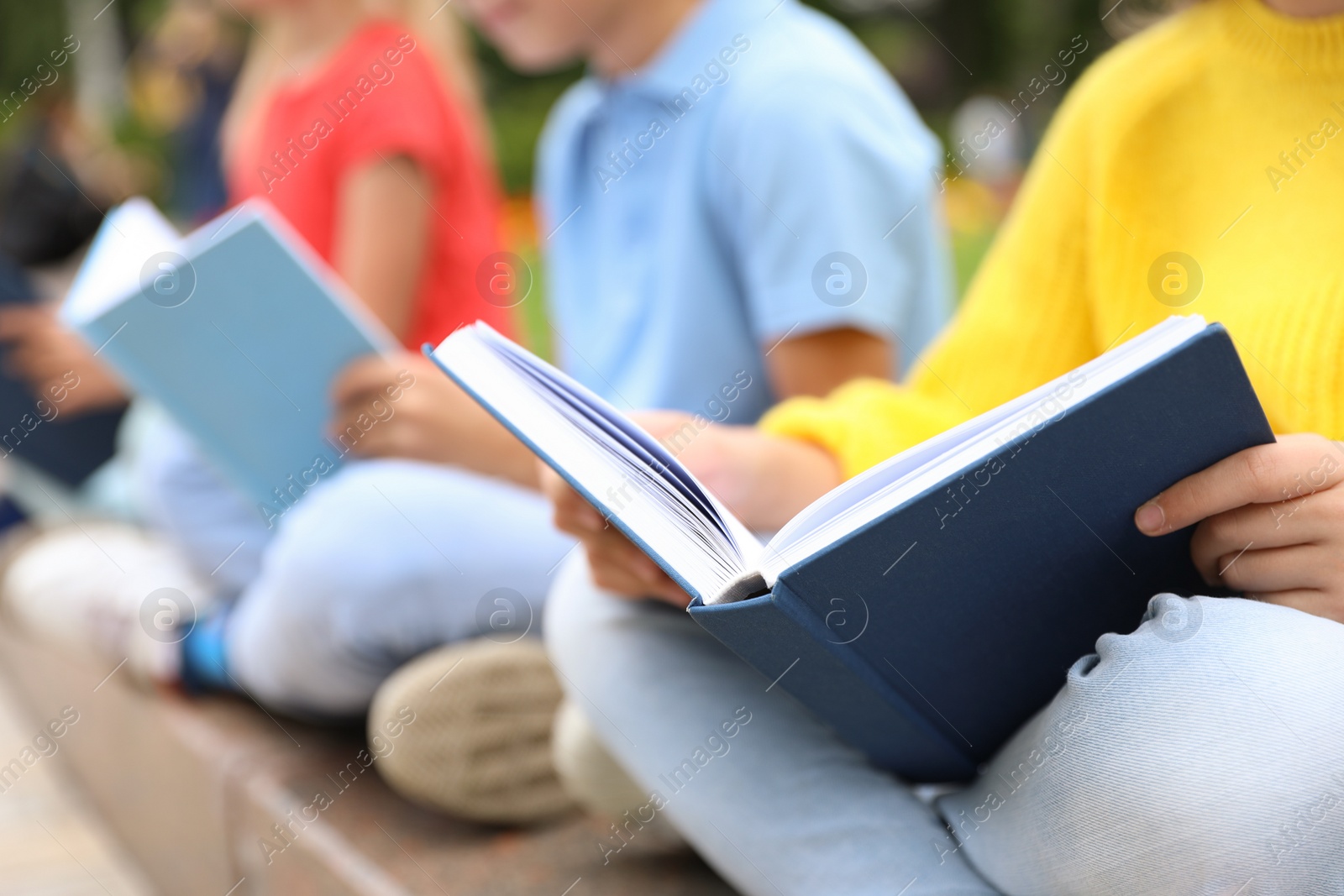 Photo of Little children reading books outdoors, closeup