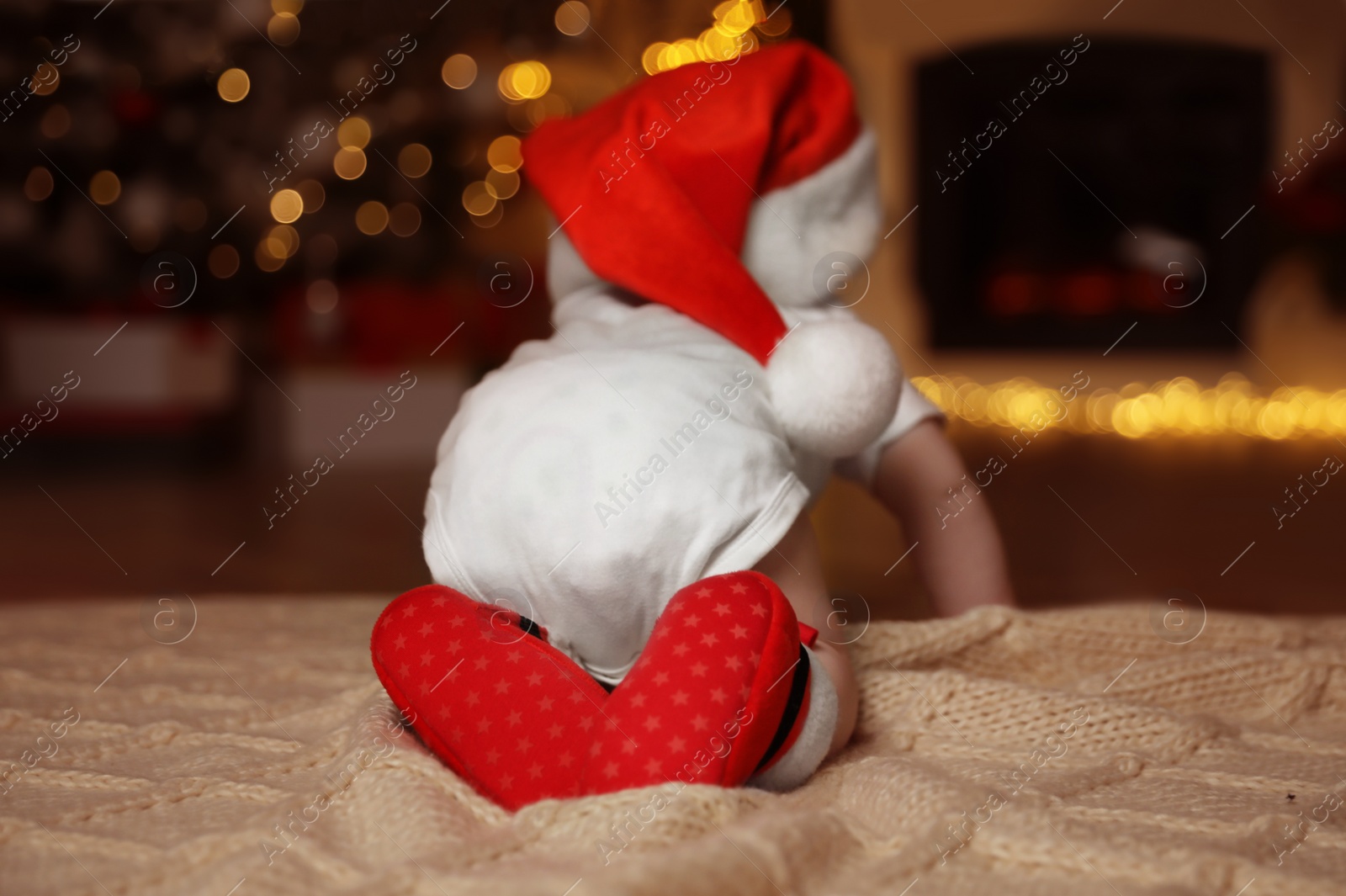 Photo of Cute little baby wearing Santa hat on blanket at home, back view. Christmas celebration