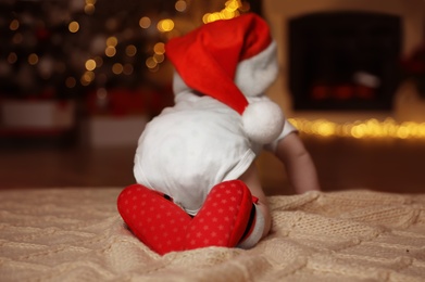 Cute little baby wearing Santa hat on blanket at home, back view. Christmas celebration