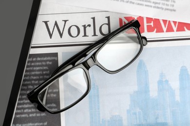 Photo of Glasses and tablet on newspapers, flat lay