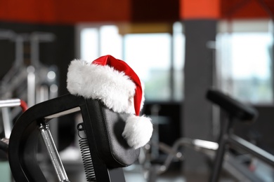 Photo of Santa Claus hat on modern exercise machine in gym