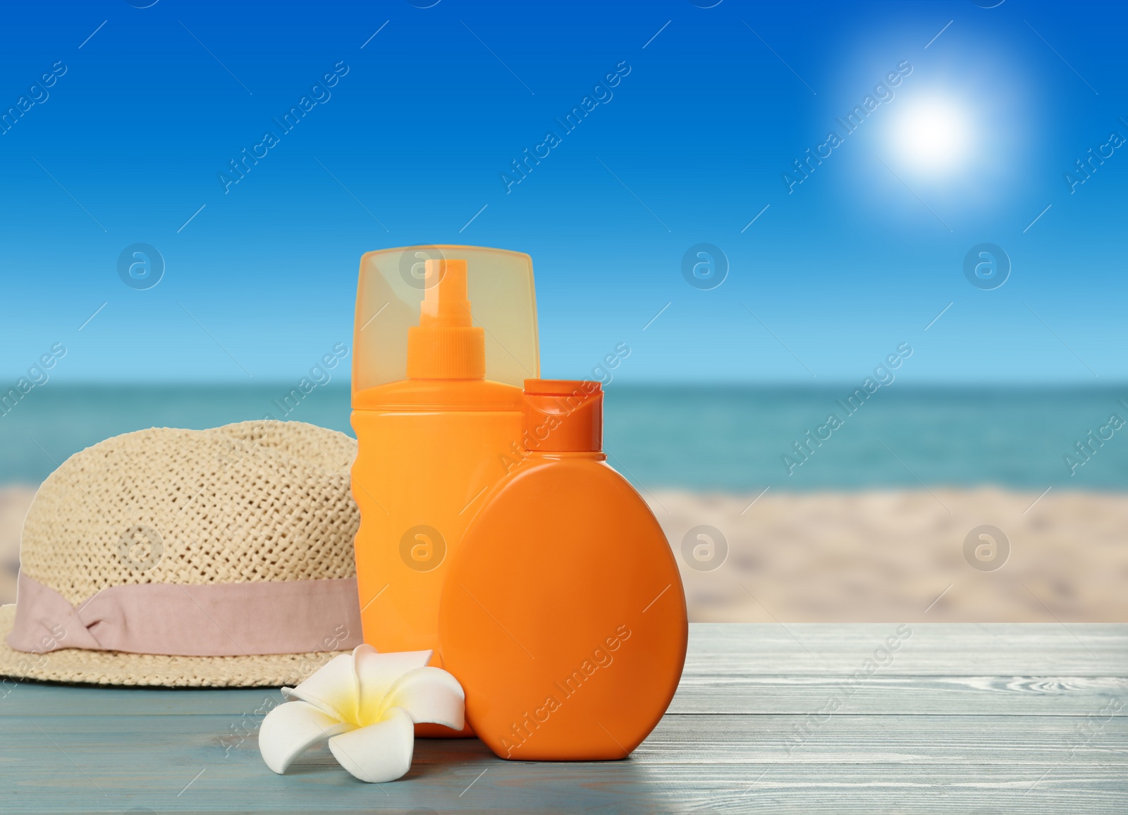 Image of Bottles of skin sun protection products and hat on light blue wooden table against seascape. Space for design