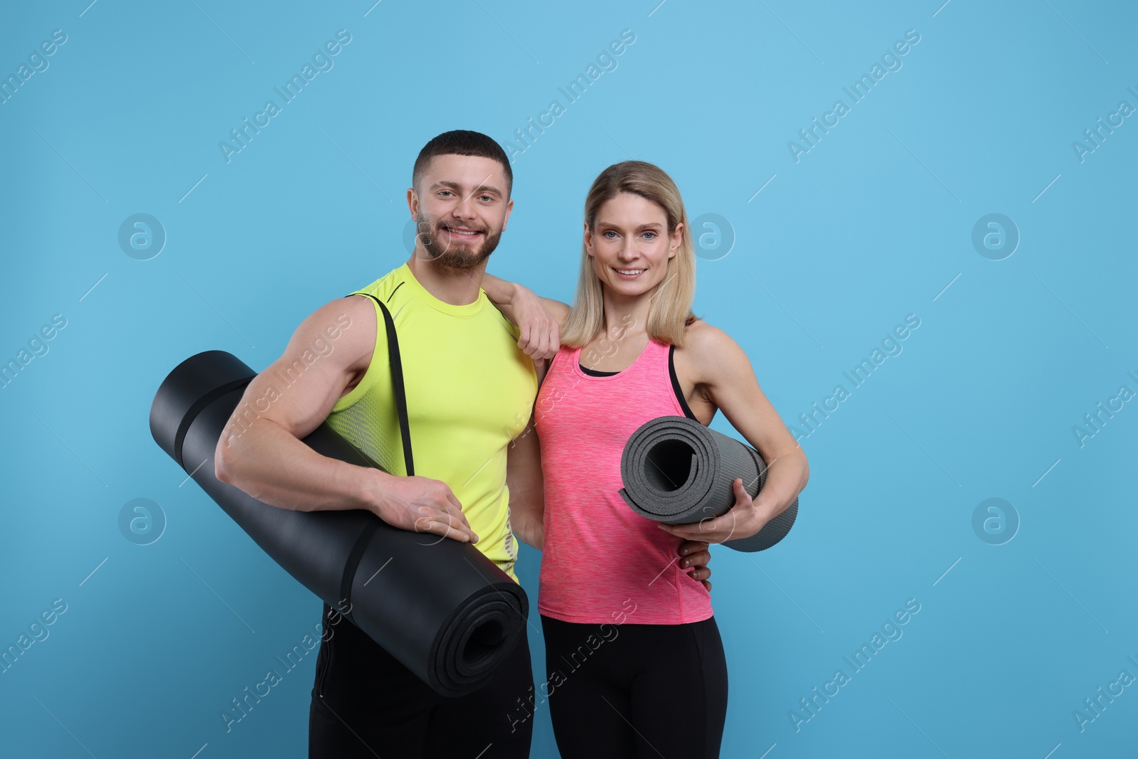 Photo of Athletic people with fitness mats on light blue background, space for text