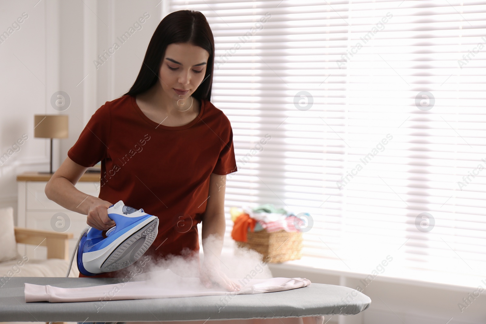 Photo of Young woman ironing clean sweatshirt at home, space for text