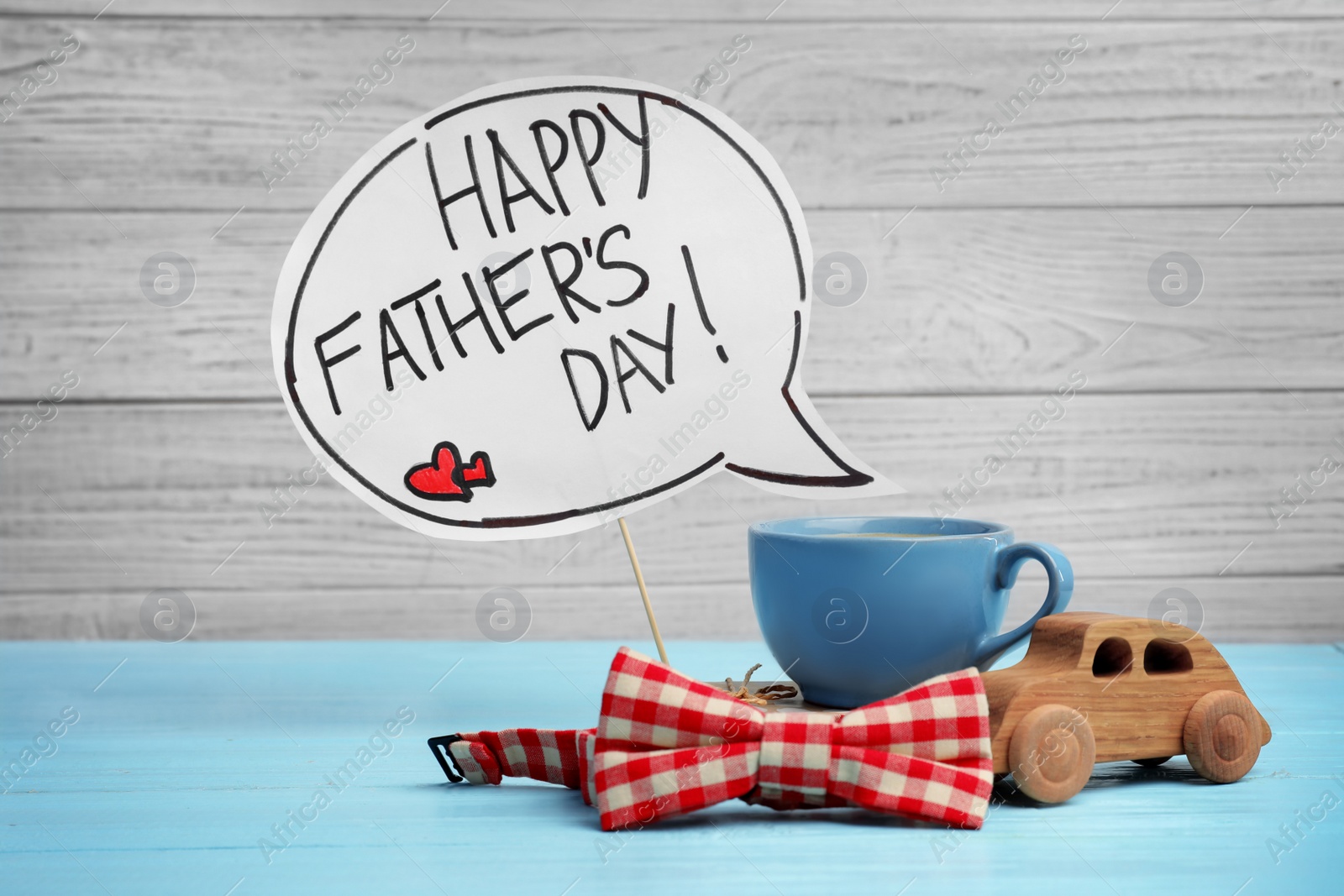Photo of Composition with words HAPPY FATHER'S DAY, toy car, cup and bow tie on wooden table