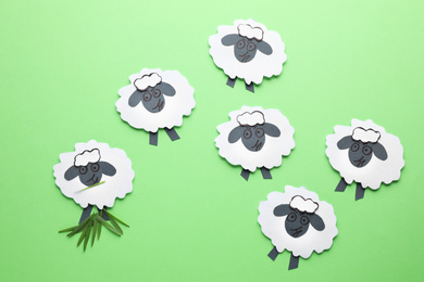 Paper sheeps on green background, flat lay. Concept of jealousy