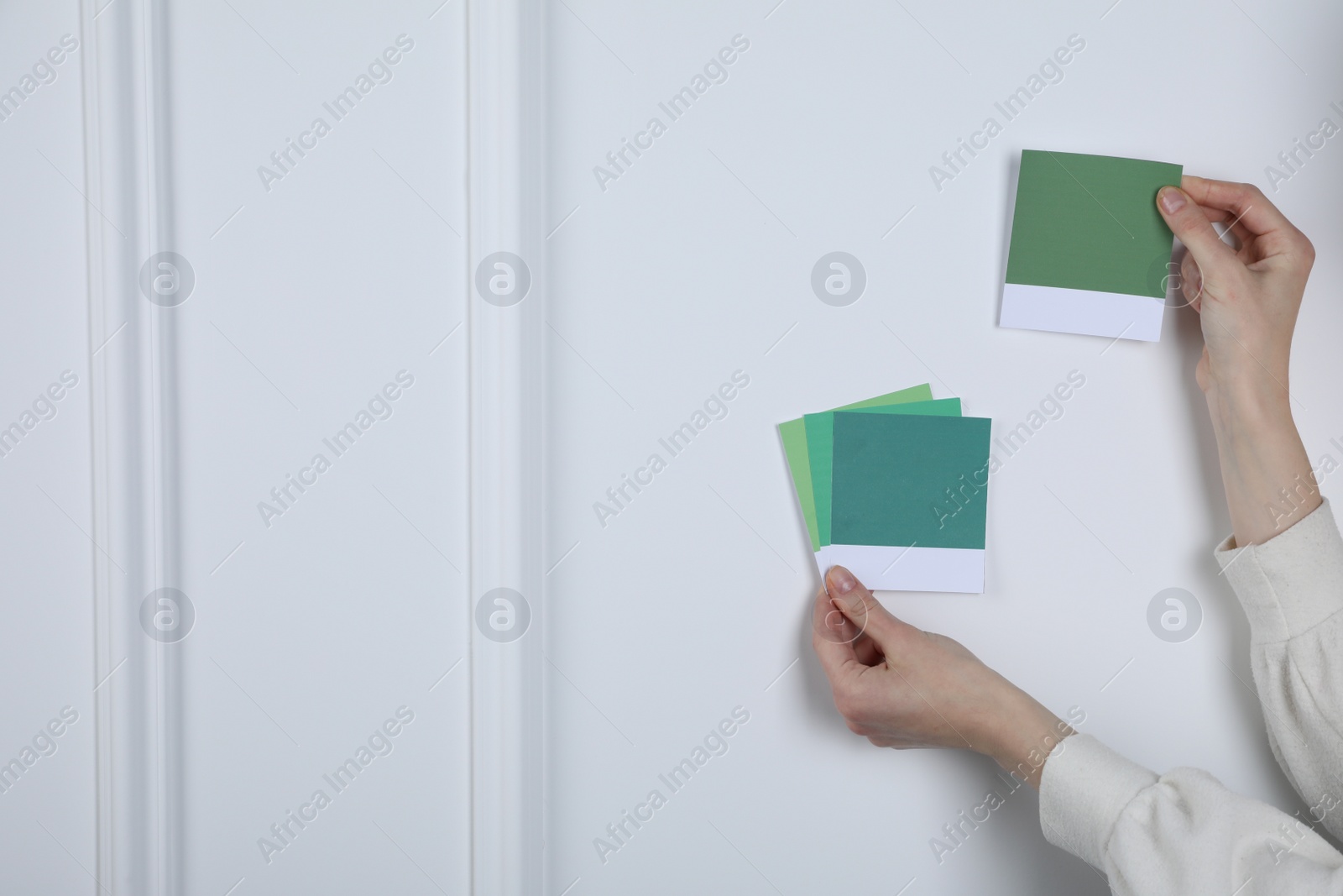 Photo of Woman with color sample cards choosing paint shade near white wall, closeup. Interior design