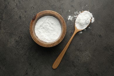 Photo of Baking powder in bowl and spoon on grey textured table, top view