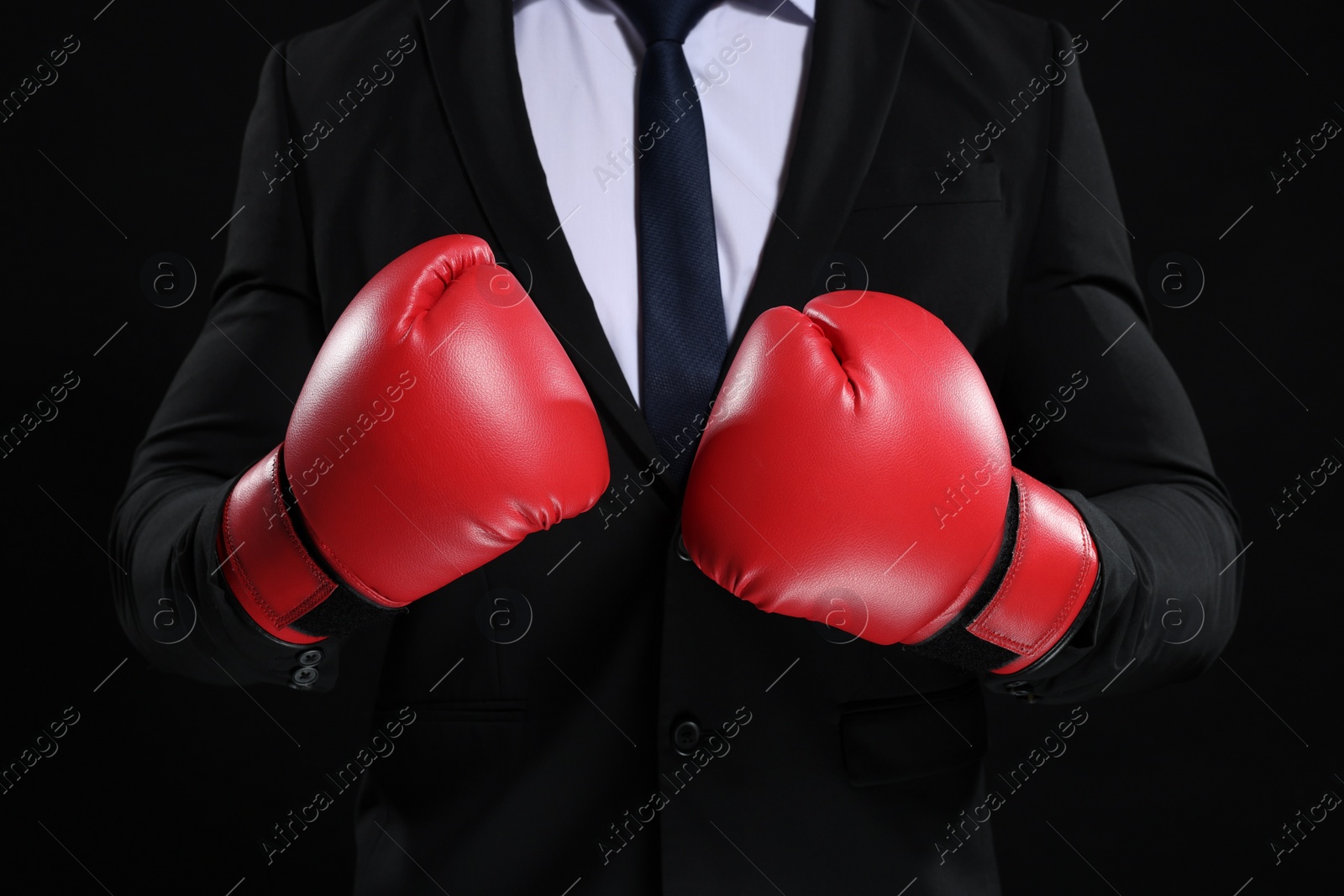 Photo of Businessman in suit wearing boxing gloves on black background, closeup