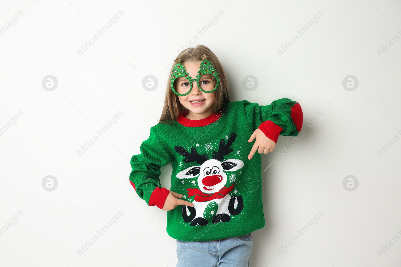 Photo of Cute little girl in Christmas sweater and party glasses on white background