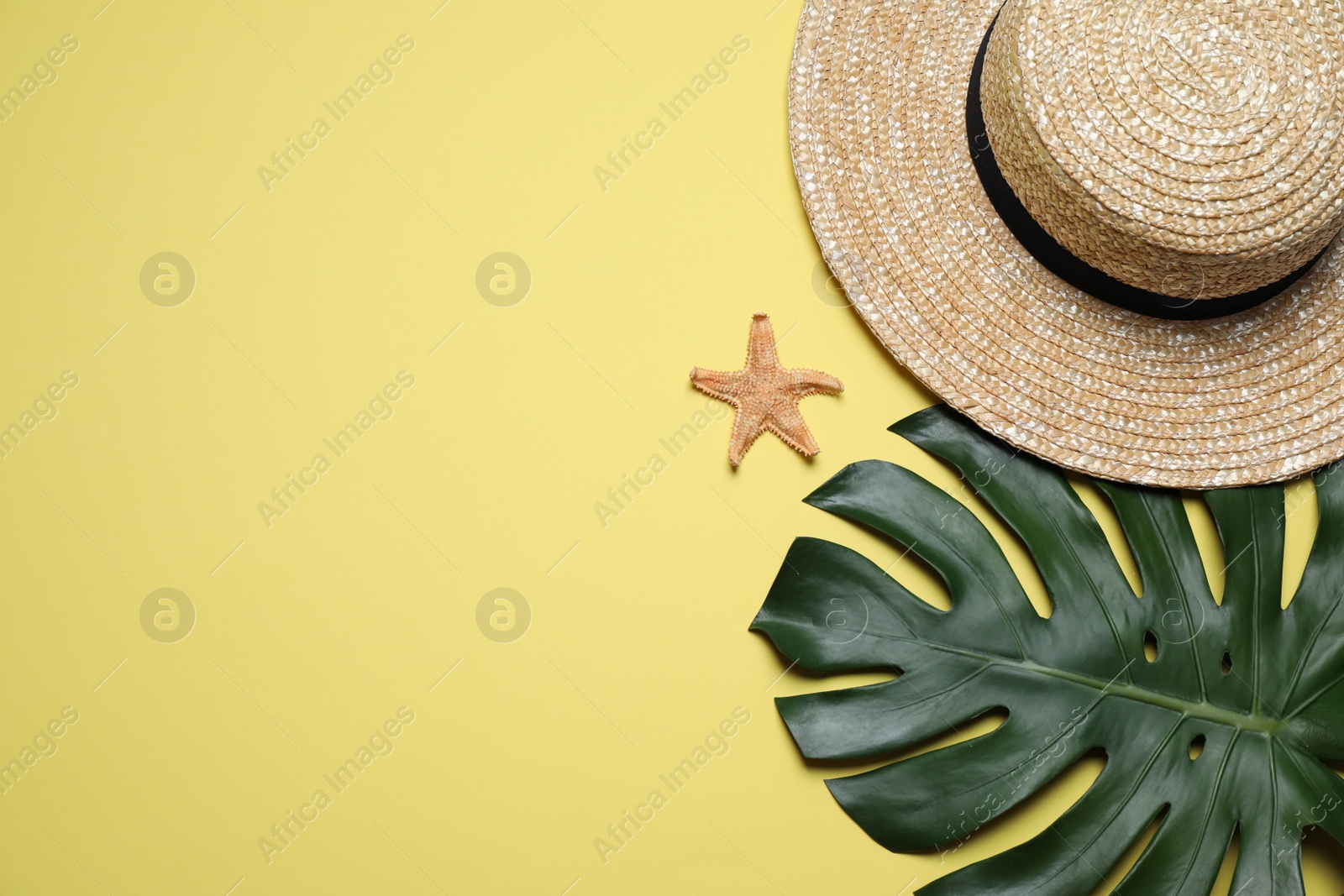 Photo of Straw hat, tropical leaf and starfish on yellow background