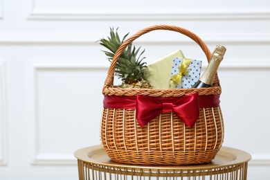 Photo of Gift set in wicker basket on golden table near white wall. Space for text