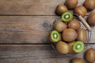 Photo of Metal basket with cut and whole fresh kiwis on wooden table, flat lay. Space for text