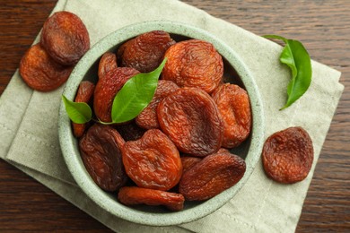 Tasty apricots and green leaves with bowl on wooden table, flat lay. Dried fruits