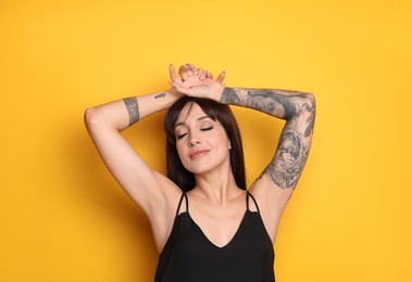 Beautiful woman with tattoos on arms against yellow background