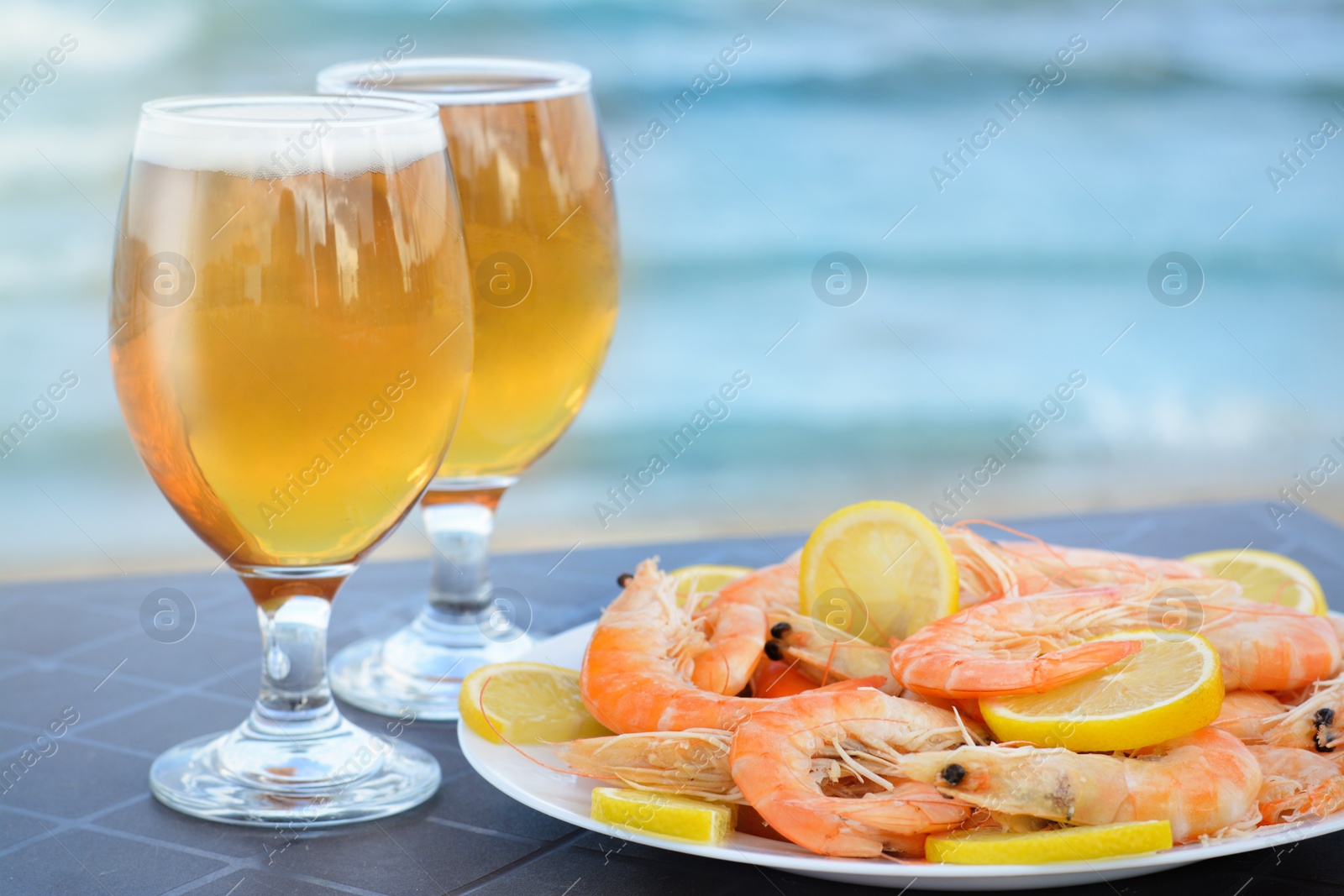 Photo of Cold beer in glasses and shrimps served with lemon on beach