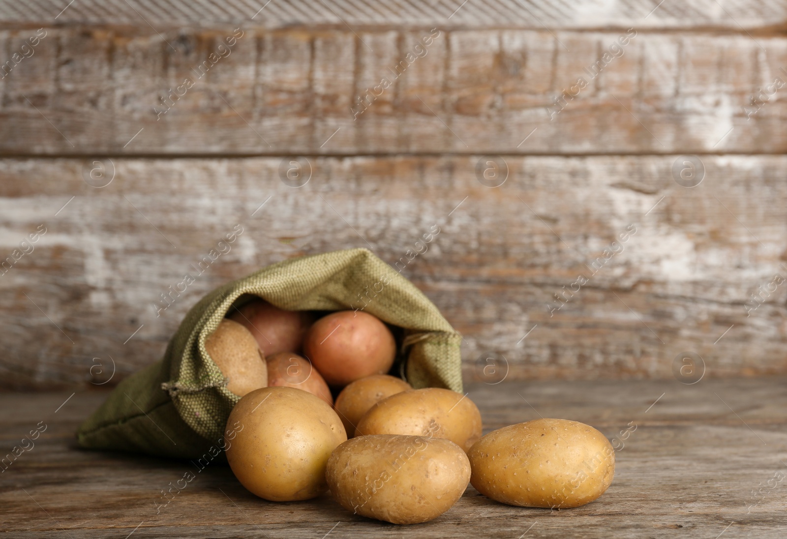 Photo of Sack with fresh ripe organic potatoes on wooden table