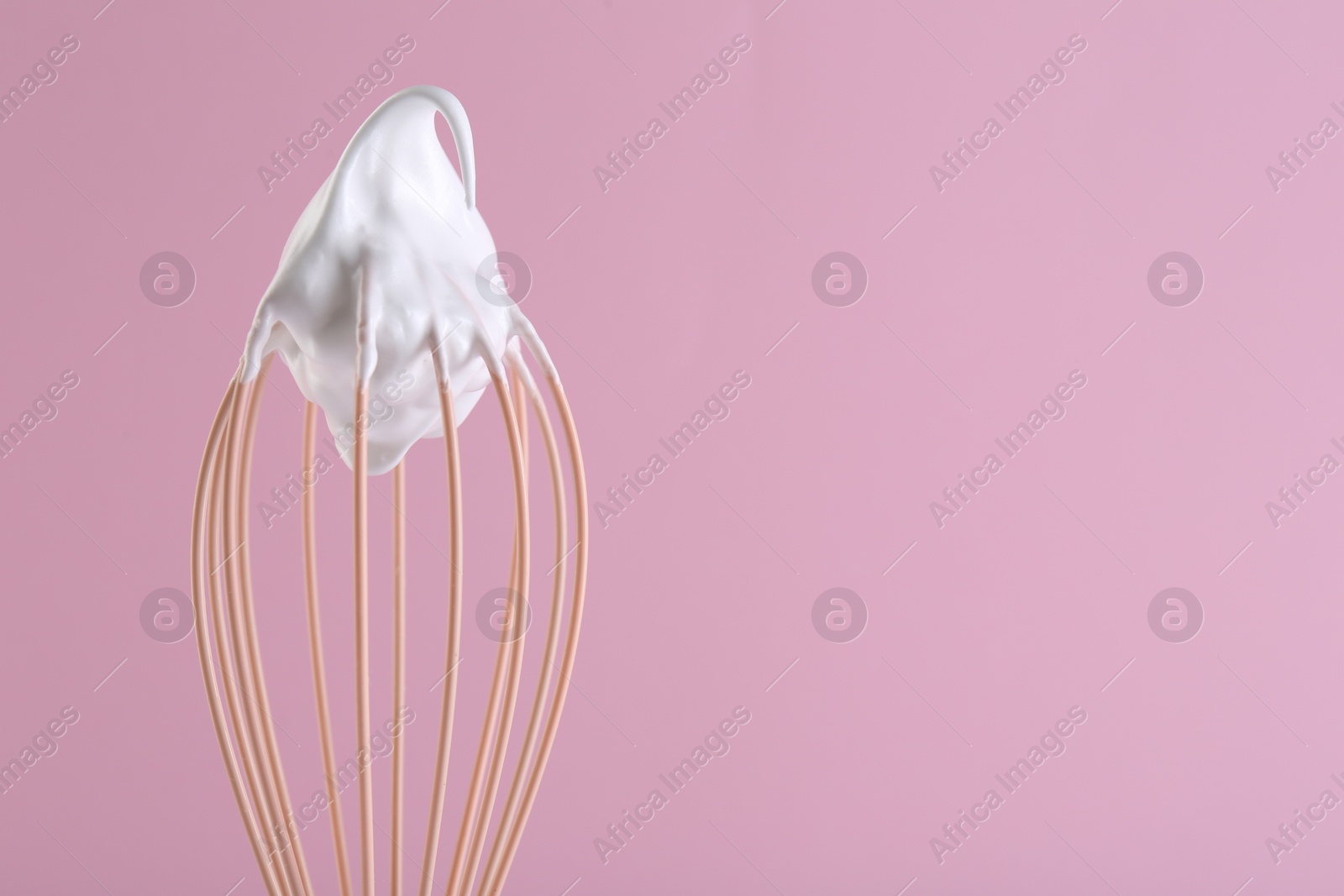 Photo of Whisk with whipped cream on pink background, closeup. Space for text