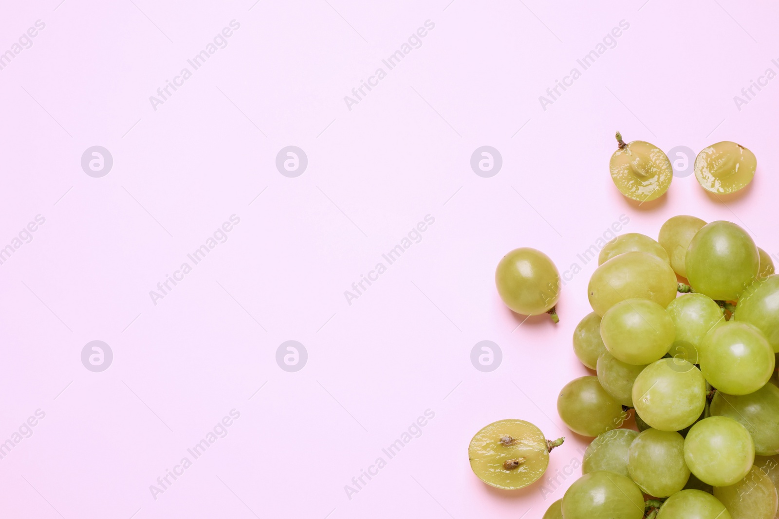 Photo of Ripe green grapes on pink background, flat lay. Space for text