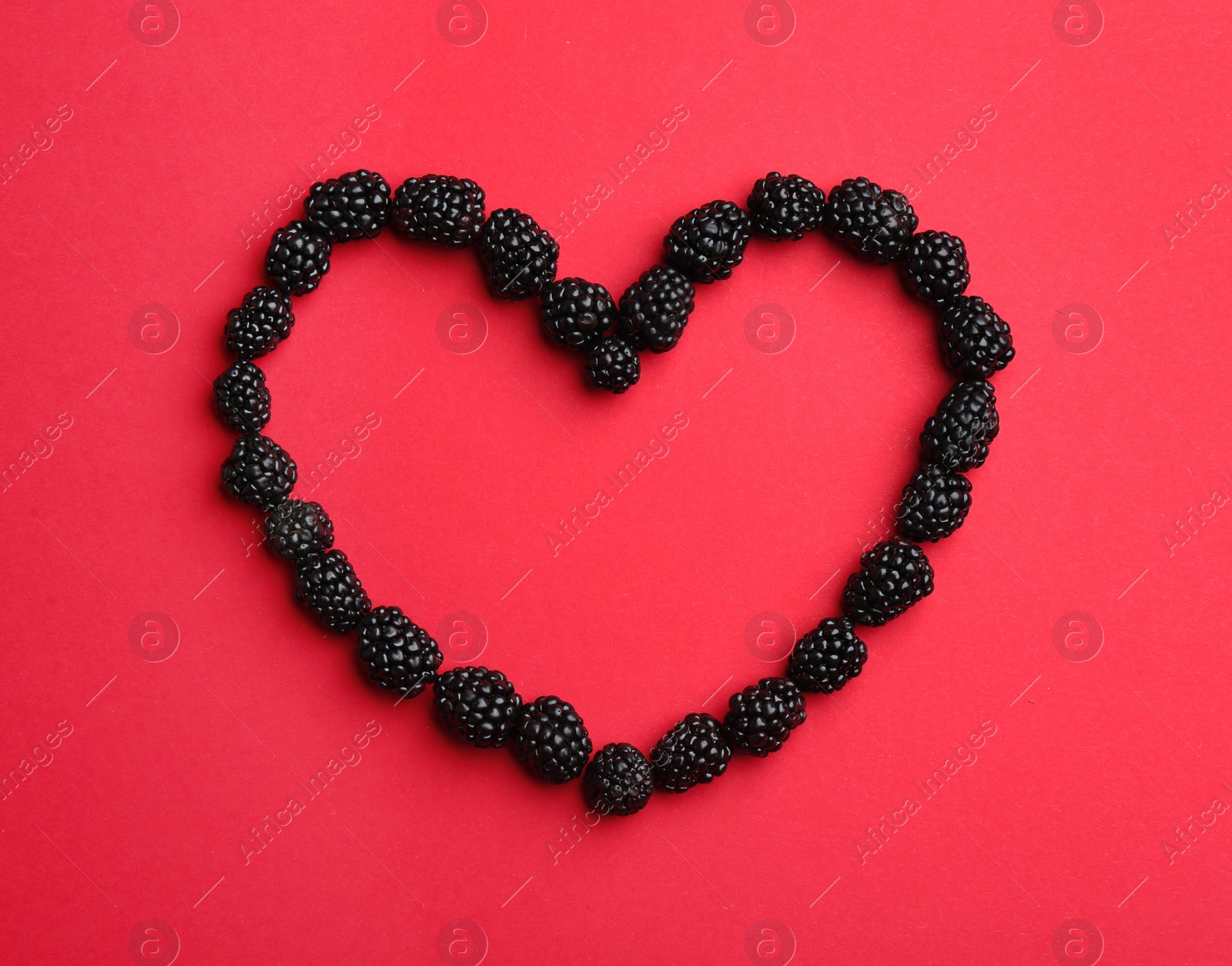 Photo of Heart shaped frame made of fresh blackberries on red background, top view. Space for text