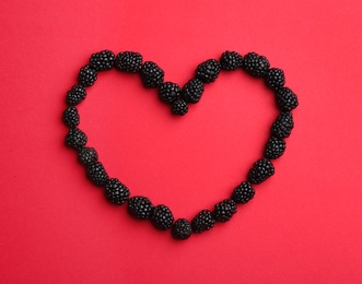 Heart shaped frame made of fresh blackberries on red background, top view. Space for text