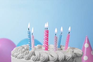 Delicious cake with burning candles and festive decor on light blue background, closeup