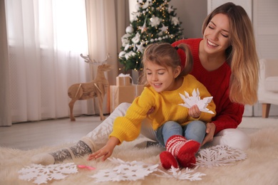 Photo of Happy mother and daughter making paper snowflake near Christmas tree at home