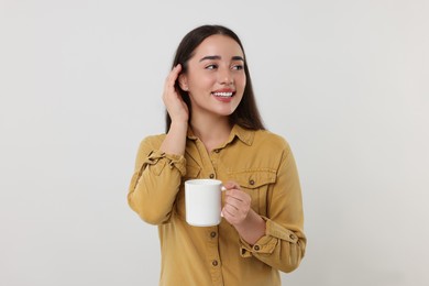 Photo of Happy young woman holding white ceramic mug on light grey background