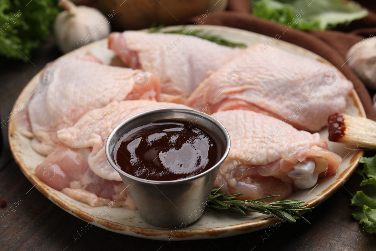 Photo of Plate with fresh marinade, raw chicken and rosemary on wooden table, closeup