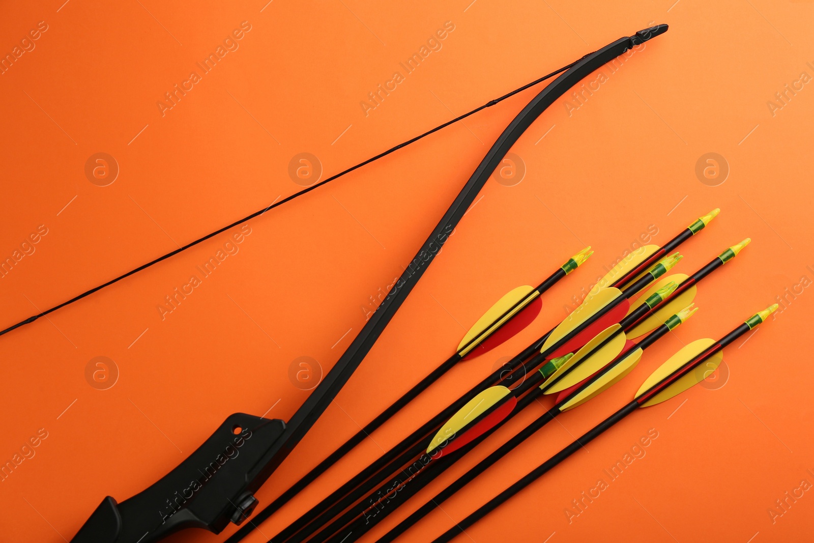Photo of Black bow and set of arrows on orange background, flat lay. Archery sports equipment