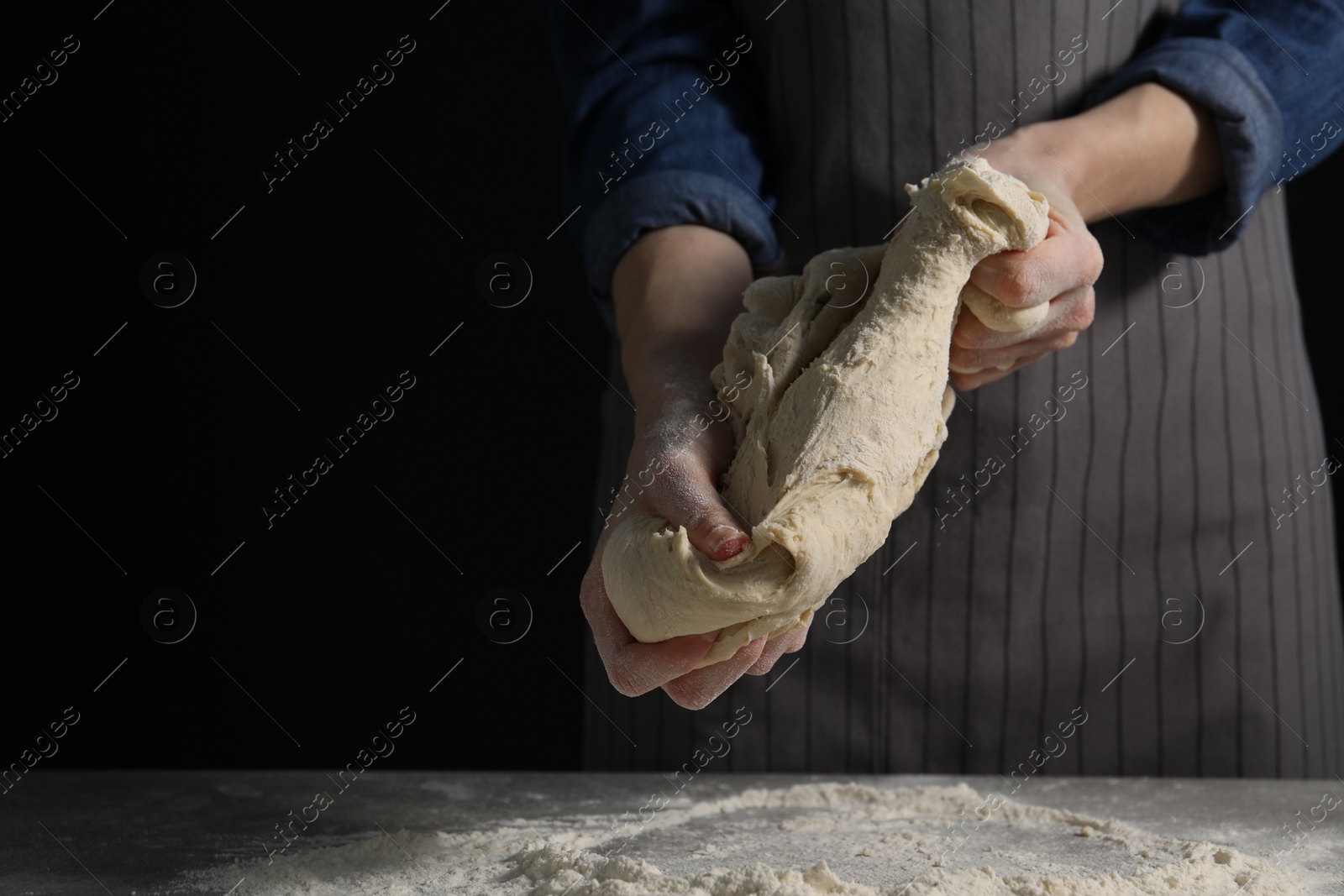 Photo of Making bread. Woman kneading dough at table on dark background, closeup. Space for text