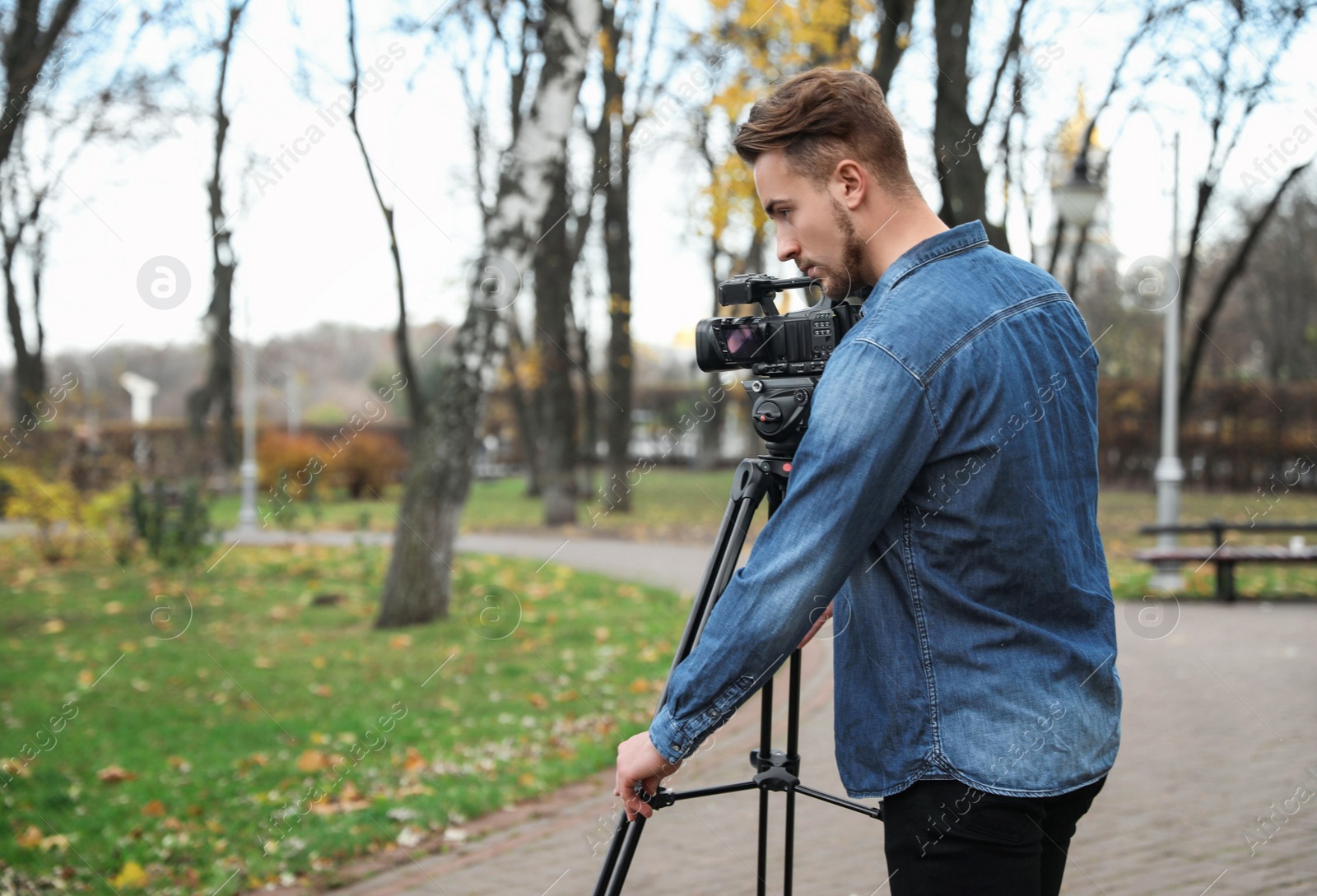 Photo of Video operator with camera working in park. Space for text