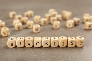 Photo of Wooden cubes with word Blacklist on grey table, closeup