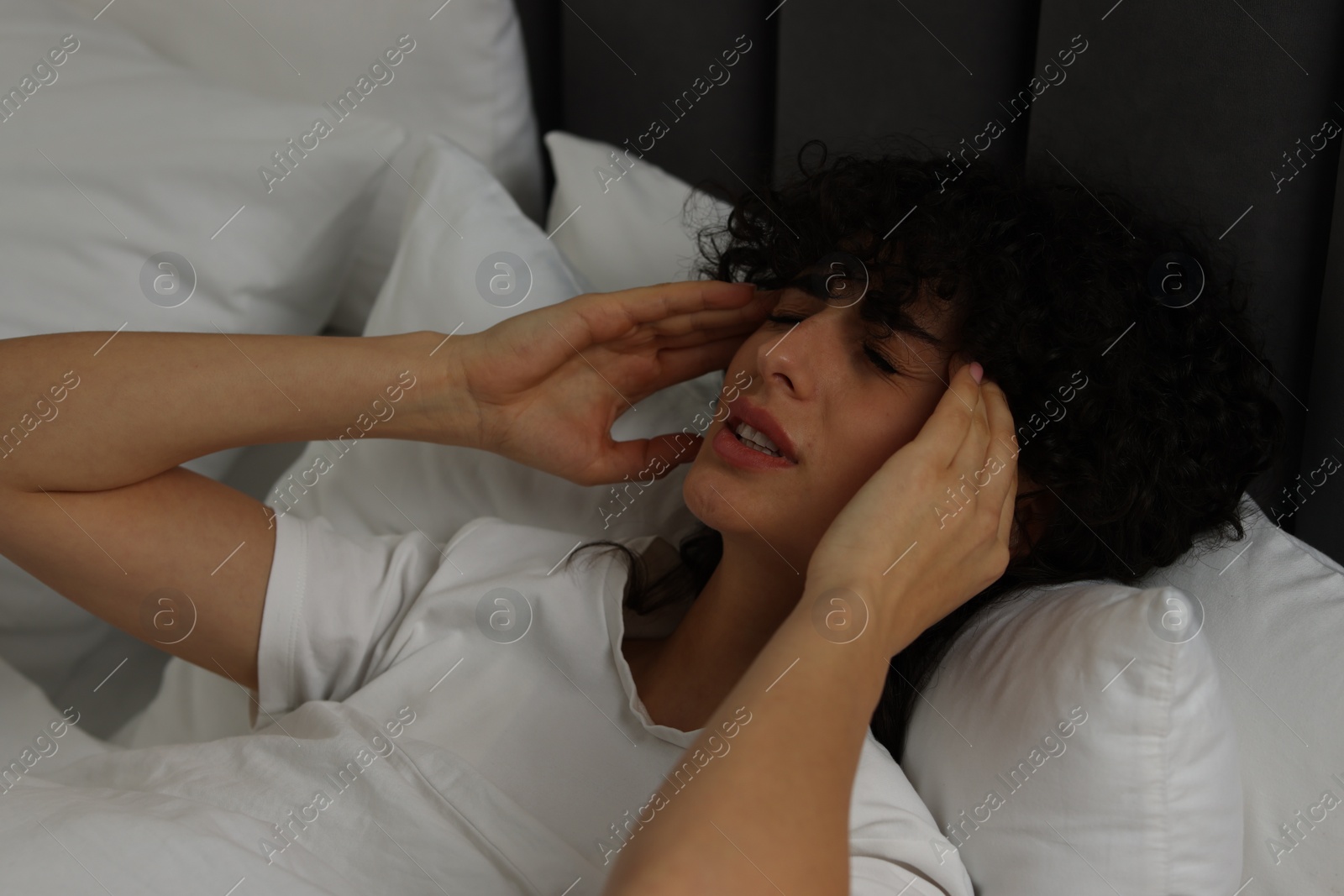 Photo of Young woman suffering from headache in bed at night