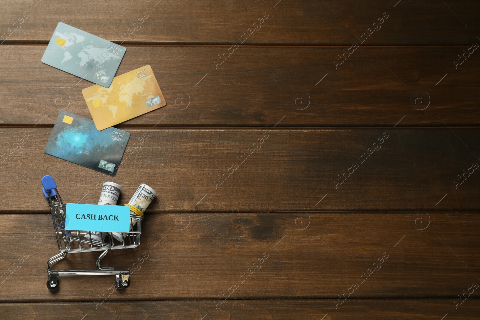 Photo of Credit cards, rolled banknotes and small shopping cart with sign Cash Back on wooden table, flat lay. Space for text