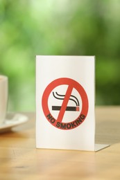 Photo of No Smoking sign on wooden table outdoors, closeup