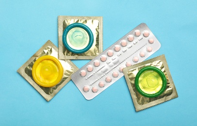 Photo of Condoms and birth control pills on light blue background, flat lay. Safe sex concept