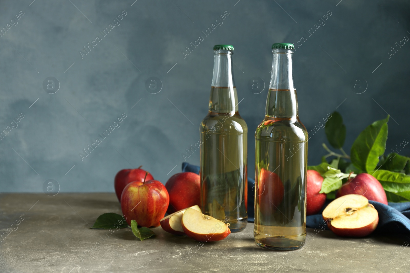 Photo of Delicious cider and apples with green leaves on gray table