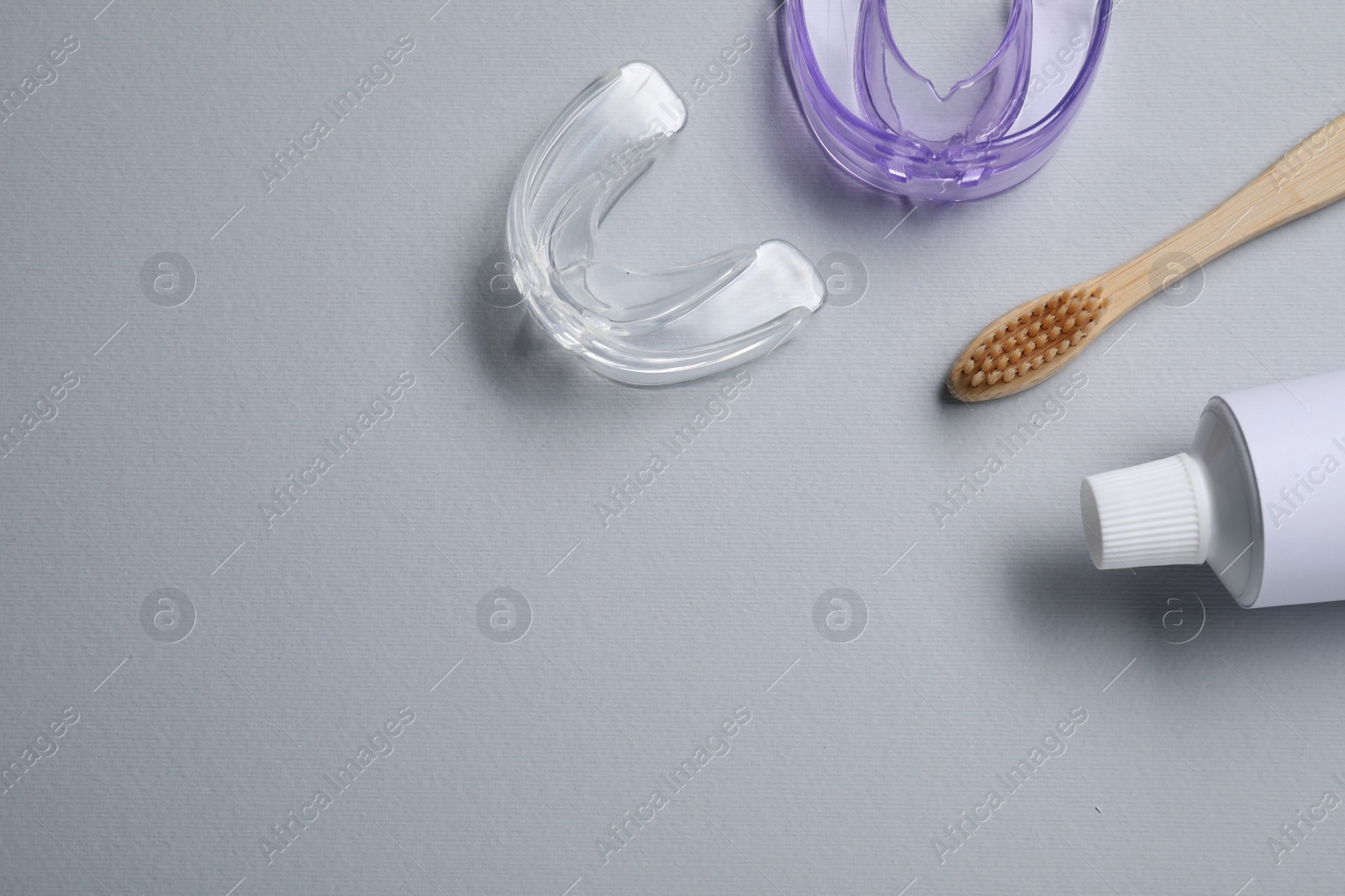 Photo of Bite correction. Toothpaste, brush and dental mouth guards on grey background, flat lay. Space for text