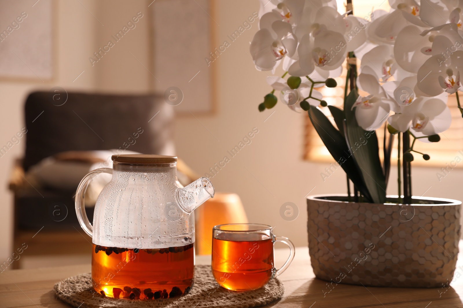 Photo of Beautiful orchid, teapot and cup with hot tea on table indoors