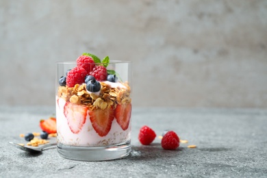 Photo of Glass of tasty homemade granola dessert on grey table, space for text. Healthy breakfast