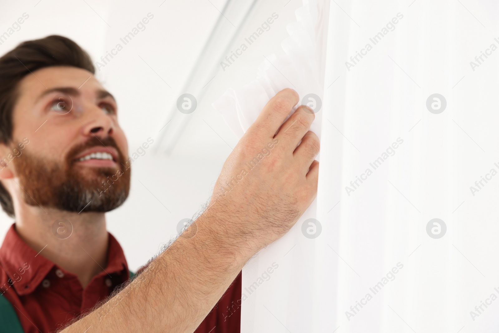 Photo of Worker in uniform hanging window curtain indoors, focus on hand