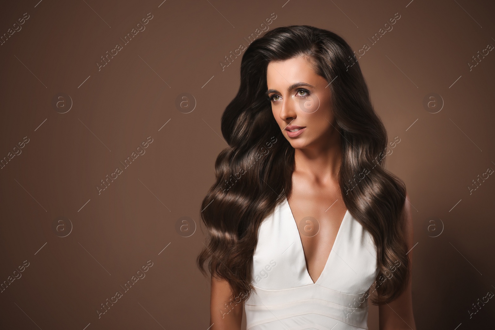 Image of Gorgeous woman with shiny wavy hair on brown background, space for text. Professional hairstyling