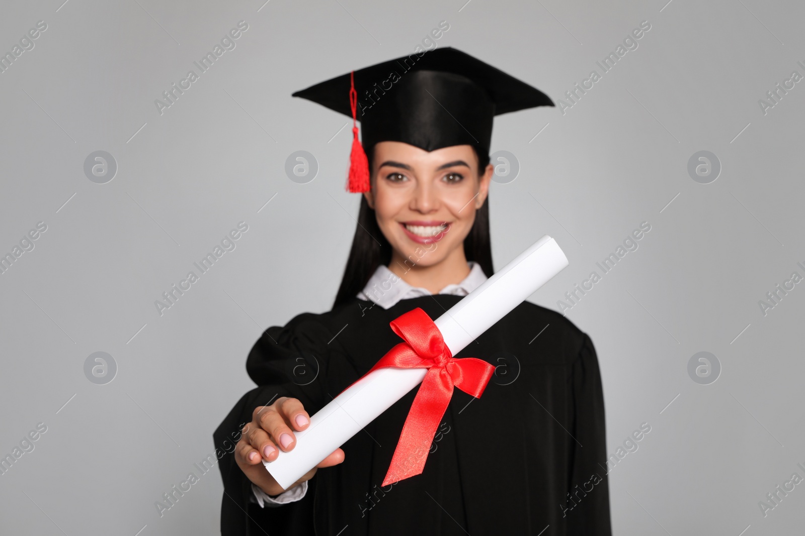 Photo of Happy student with graduation hat against grey background, focus on diploma