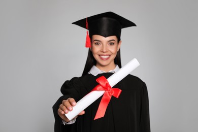 Happy student with graduation hat against grey background, focus on diploma