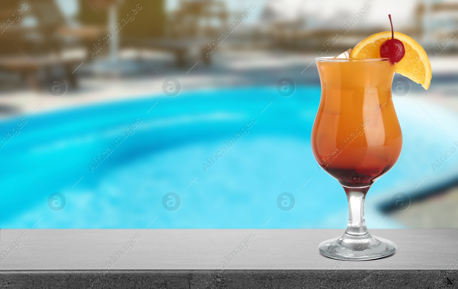 Image of Tasty refreshing cocktail on grey stone table near outdoor swimming pool, space for text