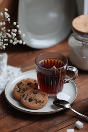 Cup of freshly brewed tea and delicious cookies on wooden table