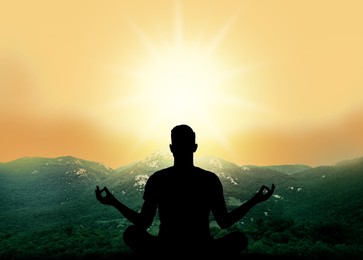 Man meditating in green mountains at sunset